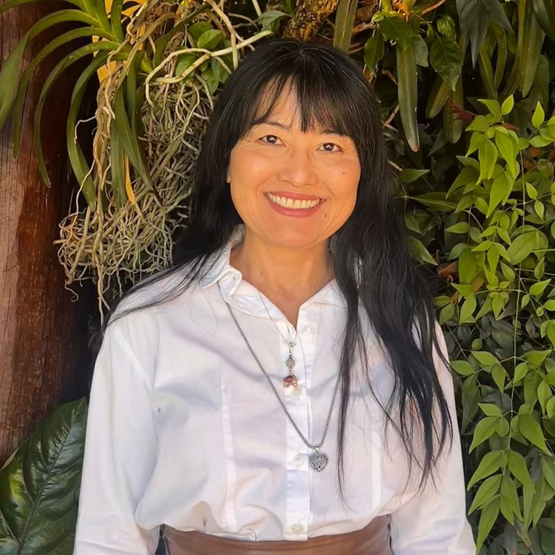 Cláudia Yumi Matsubara sorrindo com vegetação natural ao fundo